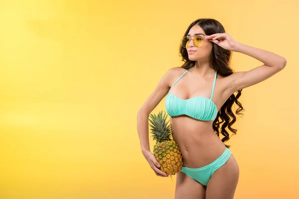 Beautiful slim girl holding fresh pineapple, isolated on yellow — Stock Photo