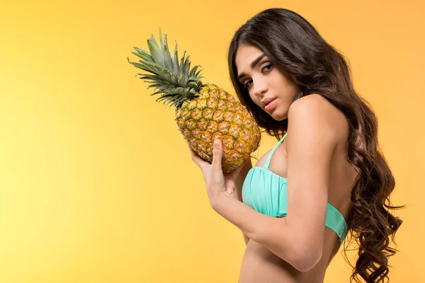Beautiful girl in bikini holding fresh pineapple, isolated on yellow — Stock Photo