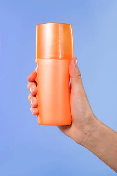 Vista ritagliata della mano femminile con bottiglia di crema solare, isolata su blu — Foto stock