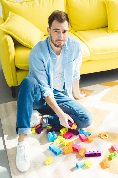 Stylish young man sitting on rug with plastic blocks — Stock Photo
