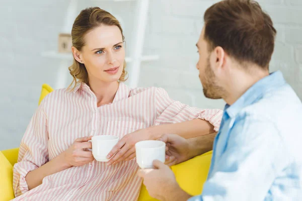 Pareja hablando y sosteniendo tazas de té en las manos - foto de stock