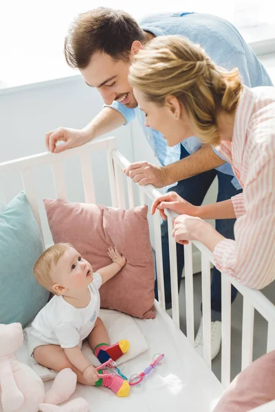 Smiling couple watching infant daughter in crib — Stock Photo
