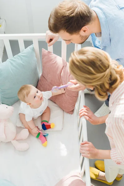 Parents playing with infant daughter sitting in crib — Stock Photo