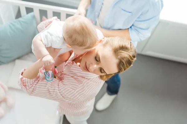 Mother raising infant daughter from crib and father standing near — Stock Photo