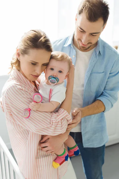 Mother holding infant daughter with baby dummy and father standing near — Stock Photo