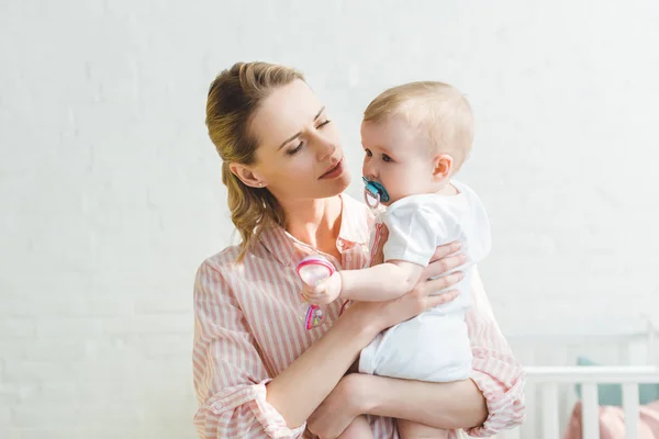 Jeune mère tenant fille bébé avec mannequin bébé et jouet à la main — Photo de stock