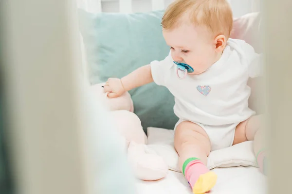 Bebé con muñeco de bebé y liebre de peluche sentado en la cuna — Stock Photo