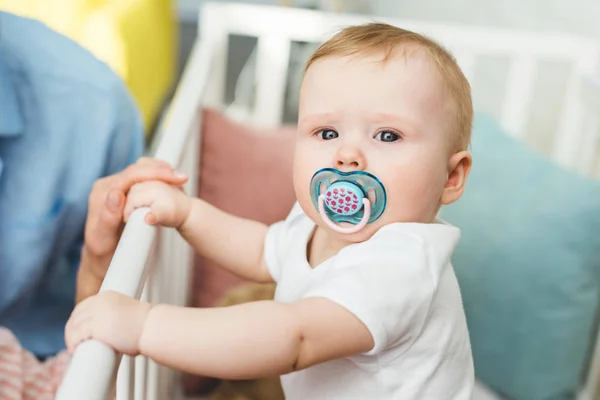 Cropped view of parents and infant daughter with baby dummy in crib — Stock Photo