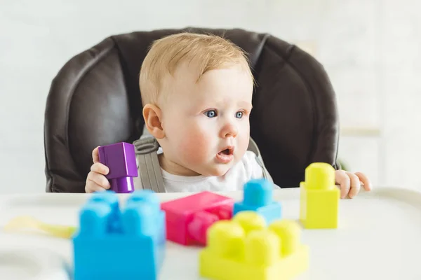 Adorable infant sititng in baby chair with plastic blocks — Stock Photo