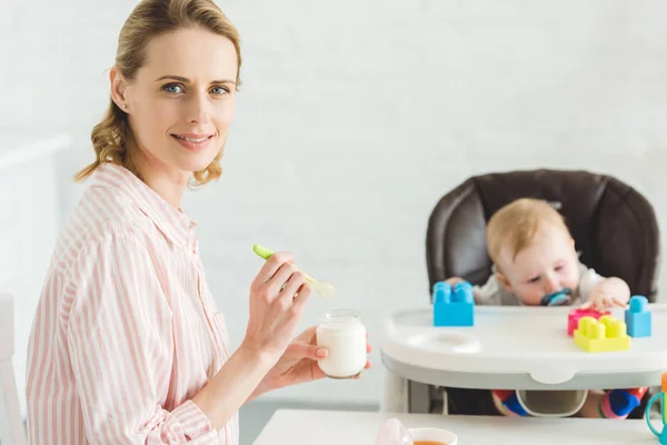 Mère avec de la nourriture et fille bébé assis dans une chaise de bébé avec des blocs en plastique — Photo de stock