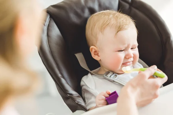 Младенец дочь в детском кресле отвергая от пищи, что мать дает ей — стоковое фото