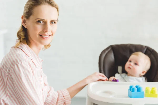Portrait of mother with infant daughter sitting in baby chair with plastic blocks — Stock Photo