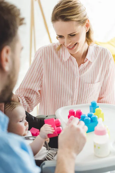 Eltern mit kleiner Tochter sitzen im Babystuhl mit Plastikblöcken und Fütterungsflasche — Stockfoto