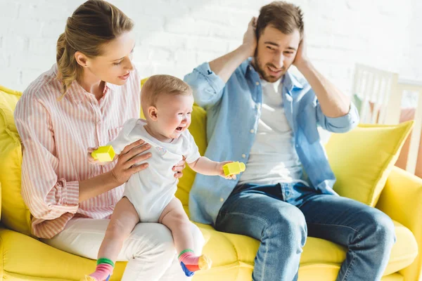 Mother triyng to calm down crying infant daughter while father shutting ears — Stock Photo