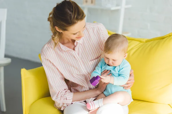 Young mother holding infant daughter with plastic block in hands — Stock Photo