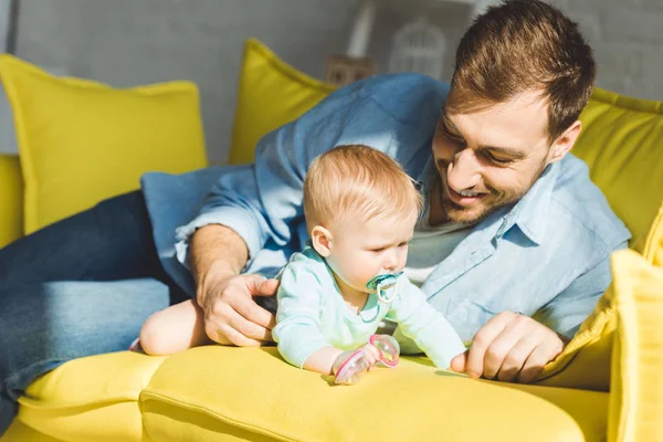Père souriant et petite fille avec mannequin bébé sur le canapé — Photo de stock