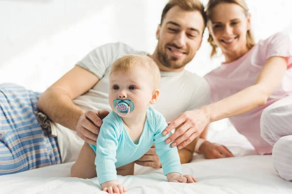 Smiling parents touching infant daughter with baby dummy — Stock Photo