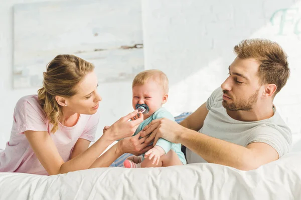 Padres jóvenes tratando de calmarse llorando hija con muñeco de bebé - foto de stock