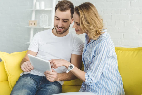 Coppia sorridente si diverte con tablet e si siede sul divano — Foto stock