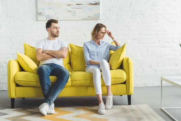 Upset couple sitting after argue on couch in front of wall with painting — Stock Photo