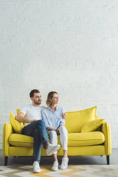Joven abrazando novia en sofá amarillo en habitación moderna - foto de stock
