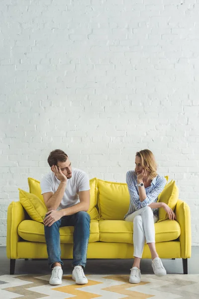 Jeune couple assis sur un canapé jaune dans une chambre moderne — Photo de stock