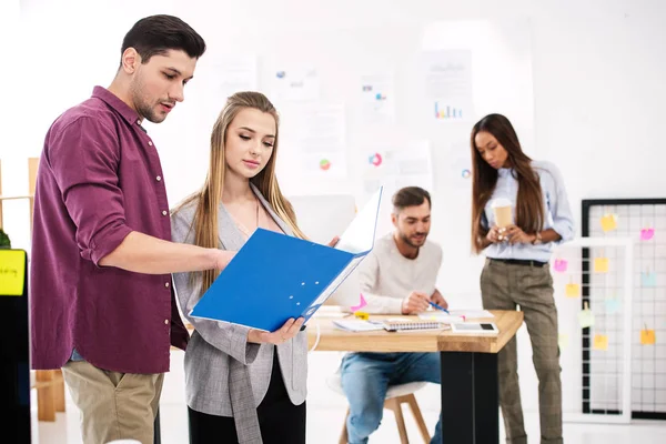 Enfoque selectivo de las personas de negocios con carpeta discutir el trabajo y colegas multiétnicos detrás en la oficina - foto de stock