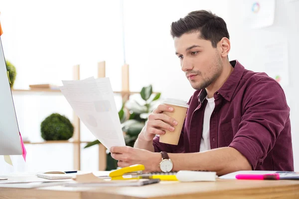 Young focused businessman with coffee to go doing paperwork at workplace in office — Stock Photo
