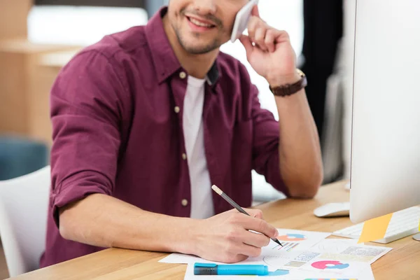 Cropped shot of smiling businessman talking on smartphone at workplace in office — Stock Photo