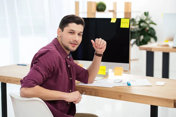 Молодой менеджер по маркетингу смотрит в камеру на рабочем месте с чистым экраном компьютера в офисе — стоковое фото