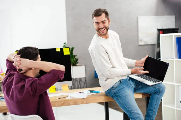 Hommes d'affaires joyeux travaillant avec ordinateur portable sur le lieu de travail ensemble dans le bureau — Photo de stock