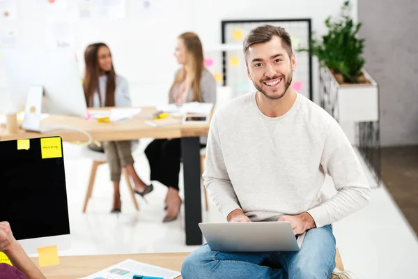 Foco seletivo de gerente de marketing sorridente com laptop sentado na mesa no escritório — Fotografia de Stock