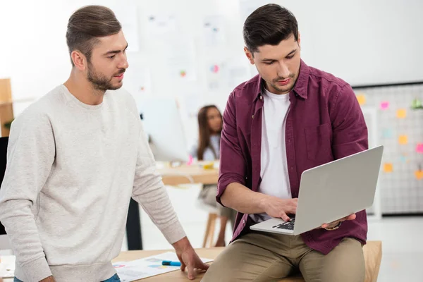 Enfoque selectivo de los jóvenes gerentes de marketing con ordenador portátil apoyado en el lugar de trabajo en la oficina - foto de stock