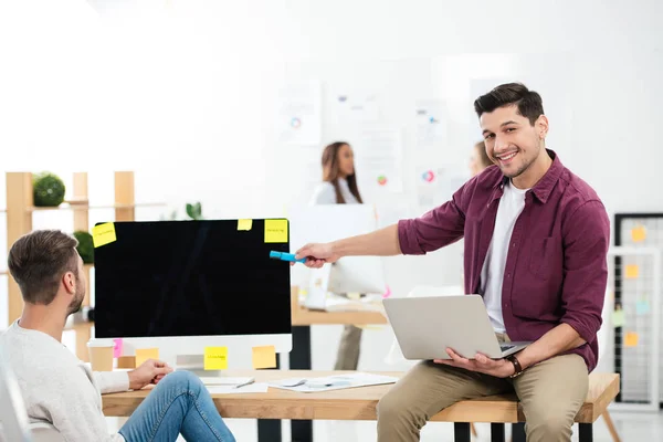 Geschäftsmann zeigt auf leeren Computerbildschirm, während er am Arbeitsplatz mit Kollegen im Büro arbeitet — Stockfoto