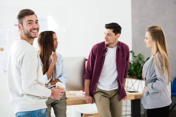 Selective focus of smiling businessman and group of young stylish multiracial business colleagues in office — Stock Photo