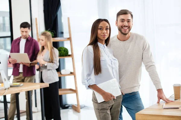 Selective focus of smiling multiracial business people with colleagues behind in office — Stock Photo