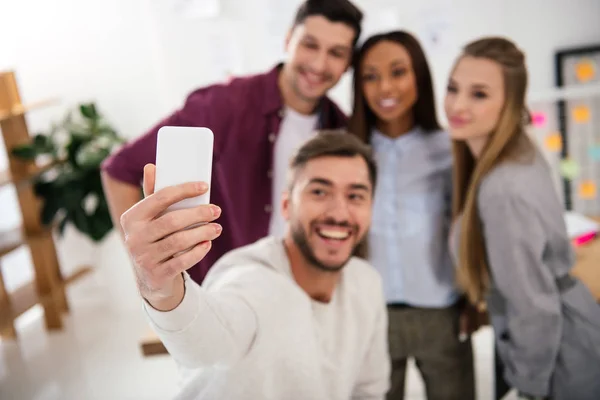 Enfoque selectivo de personas de negocios multiculturales felices tomando selfie en el teléfono inteligente juntos en la oficina - foto de stock