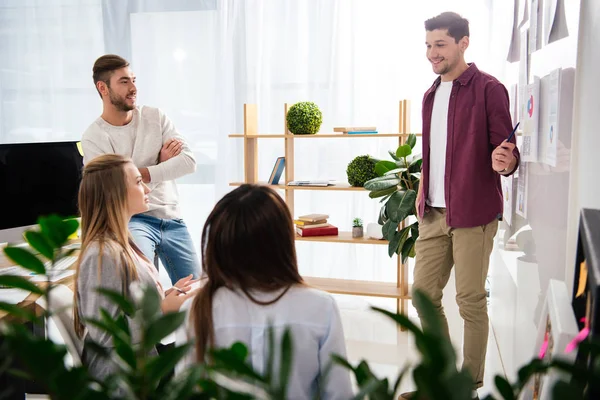 Marketing manager apuntando a pizarra blanca con documentos sobre reunión de negocios con colegas multiétnicos - foto de stock