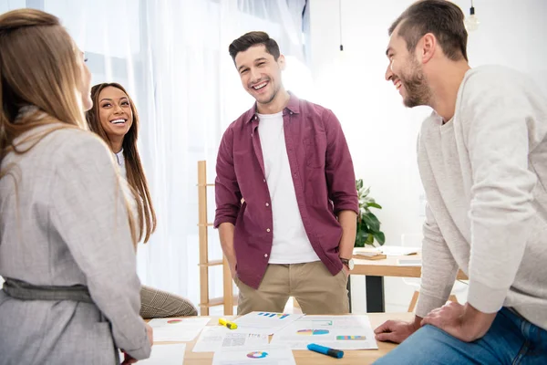 Sonrientes colegas de negocios multiétnicos discutiendo nuevo proyecto de marketing en el lugar de trabajo en la oficina - foto de stock