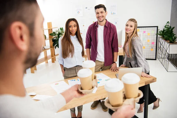 Visión parcial de empresario trajo café para ir para los colegas multiétnicos en el cargo - foto de stock