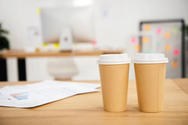 Vista de cerca de tazas de café desechables en el lugar de trabajo con papeles en la oficina - foto de stock