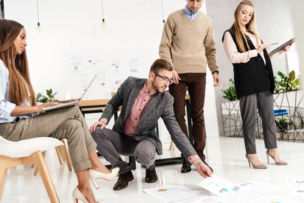 Grupo multicultural de gerentes de marketing mirando los papeles dispuestos en el piso en la oficina - foto de stock