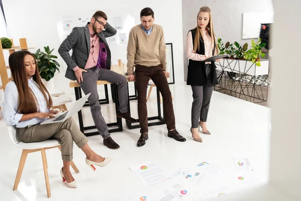 Multicultural group of marketing managers looking at papers arranged on floor in office — Stock Photo