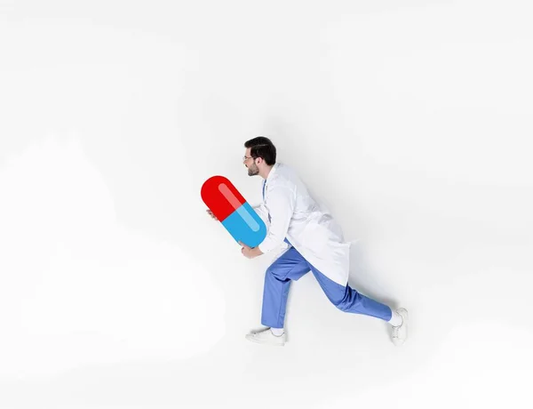 Creative collage of handsome young doctor running and holding drawn pill — Stock Photo