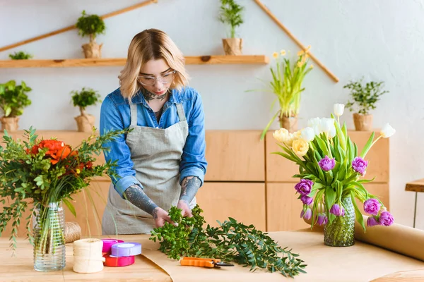 Bela florista jovem em óculos organizando flores no local de trabalho — Fotografia de Stock