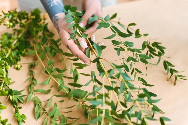 Gros plan vue partielle du fleuriste avec des mains tatouées organisant des plantes vertes sur le lieu de travail — Photo de stock