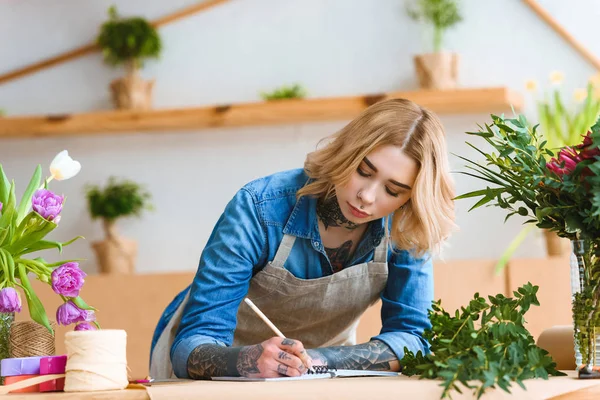 Schöne junge Floristin macht sich Notizen am Arbeitsplatz — Stockfoto