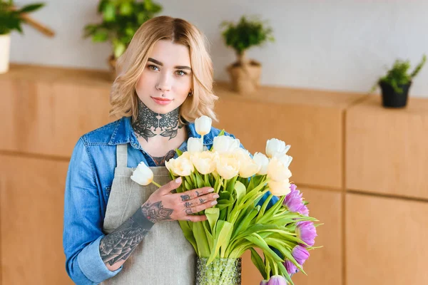 Молода жінка-квітка в фартусі тримає красиві тюльпани у вазі і дивиться на камеру — стокове фото