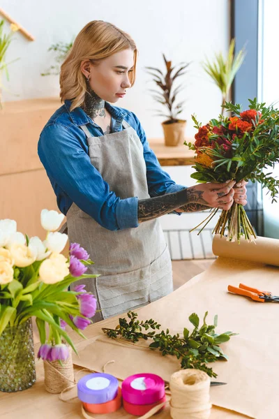 Fokussierte junge Floristin in Schürze hält schönen Strauß im Blumenladen — Stockfoto