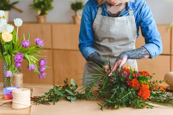 Tiro recortado de florista joven en delantal trabajando con flores - foto de stock